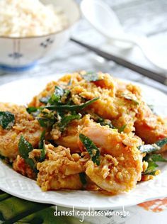 a white plate topped with fried food next to a bowl filled with rice and vegetables