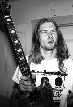 a man with long hair holding an electric guitar in his right hand and looking at the camera