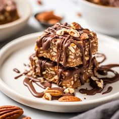 a white plate topped with three pieces of cake covered in chocolate and pecan nuts