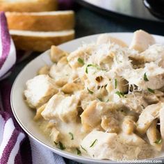 a white plate topped with pasta and meat covered in gravy next to bread