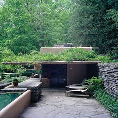 an outdoor swimming pool surrounded by greenery and stone walls, with lounge chairs around it