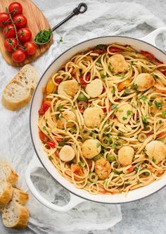 pasta with scallops and tomatoes in a pan on the table next to bread