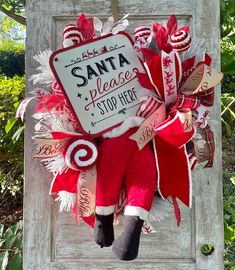 a christmas wreath with santa's please stop here sign hanging on an old door