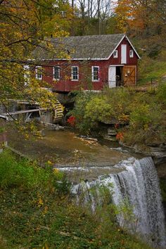 a red house sitting on top of a lush green hillside next to a small waterfall