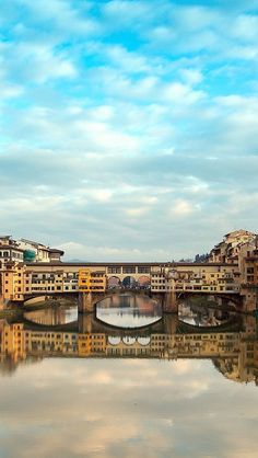 a bridge over a body of water with buildings on both sides and clouds in the sky