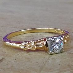 a yellow gold ring with a princess cut diamond in the center, on a wooden surface