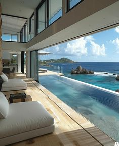 a living room filled with white furniture next to an ocean side pool on top of a wooden floor