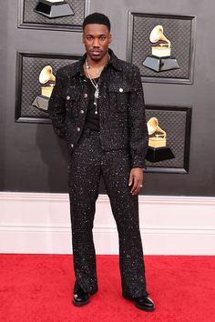 a man standing on top of a red carpet wearing a black suit and silver shoes