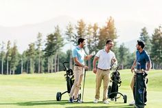 three men standing on a golf course talking to each other and holding golf clubs in their hands