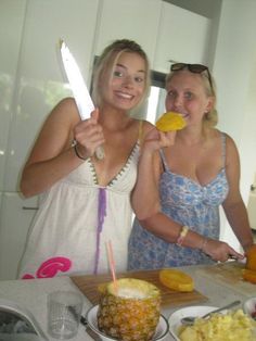 two women standing in front of a cutting board with pineapples on it and one holding a knife