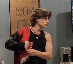 a young man is standing in front of a coffee machine and looking at something on the wall