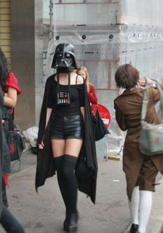 a woman dressed as darth vader is walking down the street with other people