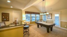 a pool table in the middle of a living room with two chairs and a bar