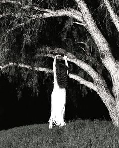 black and white photograph of a woman reaching up to a tree with her arms in the air