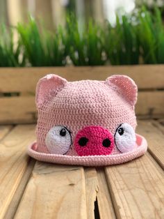 a crocheted pig hat sitting on top of a wooden table next to grass