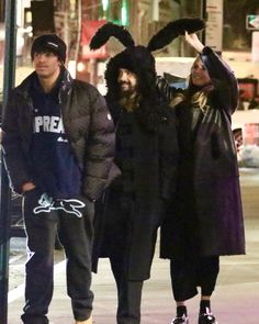 three people in bunny ears are walking down the street with one person wearing a costume