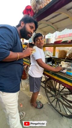 a man standing next to a little boy near a cart with food on top of it