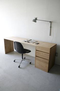 an office desk with two drawers and a lamp on the wall above it, in a white room