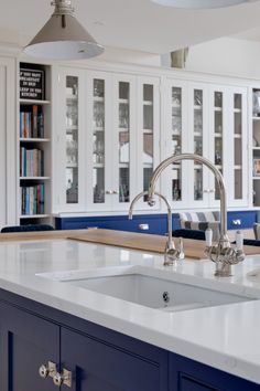 a kitchen with blue cabinets and white countertops is pictured in this image, the sink has two faucets on it