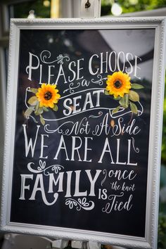 a chalkboard sign with sunflowers on it that says please choose seat not a side, we are all family