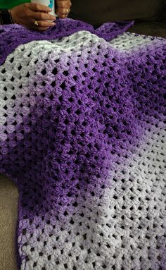 a woman is holding a purple and white crocheted blanket