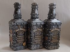 three bottles are sitting next to each other on a white tablecloth covered surface, one is made out of metal and the other has steampunk