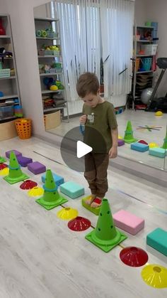 a young boy standing on top of a wooden floor next to colorful blocks and cones