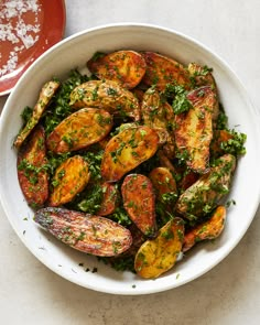 a white bowl filled with cooked potatoes covered in herbs and seasoning next to a red sauce