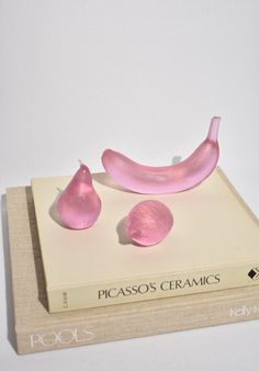 a pink object sitting on top of a book next to a peeled banana and two pieces of fruit