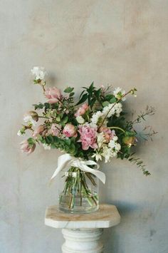 a vase filled with pink and white flowers on top of a wooden table next to a wall