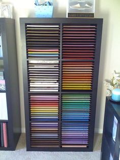 a bookcase filled with lots of different colored papers next to a black cabinet in a room