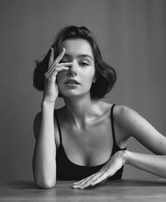 a black and white photo of a woman sitting at a table with her hand on her face