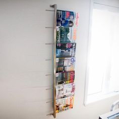 a magazine rack is hanging on the wall next to a window in a white room