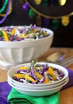 two white bowls filled with salad on top of a wooden table next to purple and green napkins