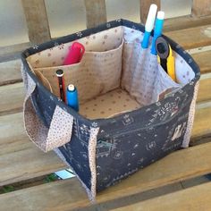 a bag that is sitting on top of a wooden bench with some pens and pencils in it