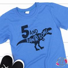 a t - shirt with the number five and a dinosaur on it is next to a pair of black shoes