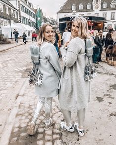 two women standing next to each other in front of a crowd on a cobblestone street