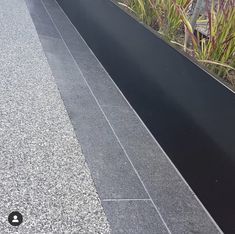 a black metal planter sitting on the side of a road next to grass and plants