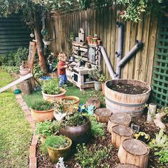 a little boy standing next to a wooden barrel filled with plants and potted plants