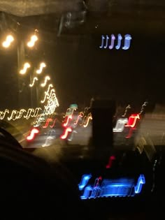 blurry photograph of cars driving at night with colorful lights on the street and trees in the background