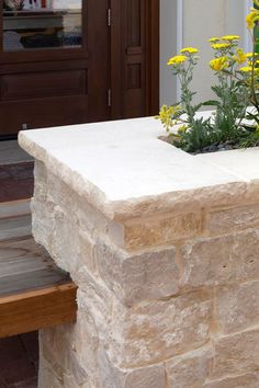 a planter with yellow flowers is sitting on a stone wall near a wooden bench