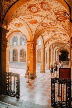 people are walking around in an old building with arches and paintings on the walls,