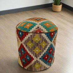 a multicolored ottoman sitting on top of a hard wood floor next to a potted plant