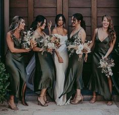 a group of women standing next to each other in front of a wooden door holding bouquets