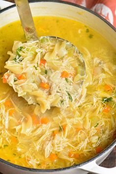 a ladle full of chicken noodle soup with carrots and parmesan cheese