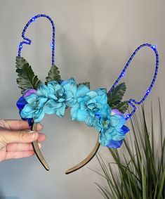 a hand holding a blue flower decorated headband