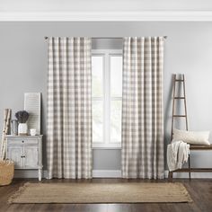 a living room with white walls and wooden flooring, gray plaid curtains, an area rug