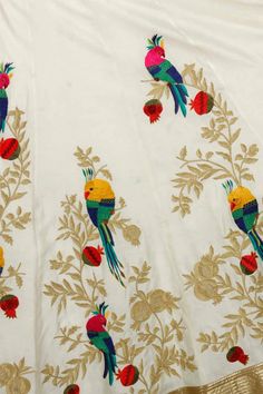 an embroidered white cloth with colorful birds on it and gold trim around the neckline