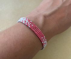 a person wearing a red and white beaded bracelet on their arm with a blue wristband