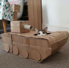 a cat laying in a cardboard tank on the floor